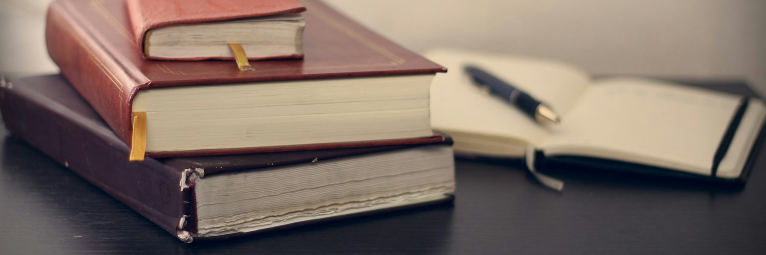 Aufgeschlagenes Notizbuch neben gestapelten Büchern